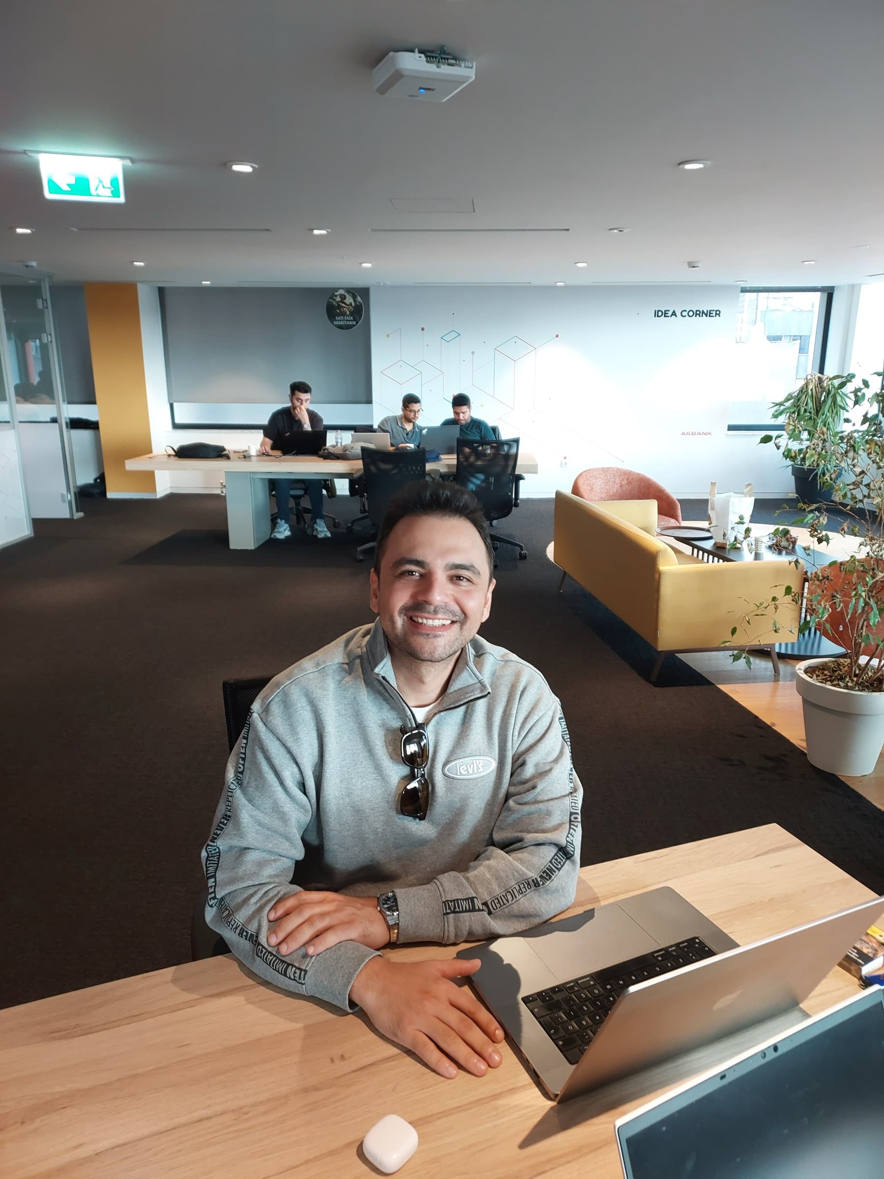 Yunus Emre smiling at his laptop in a bright open-plan office