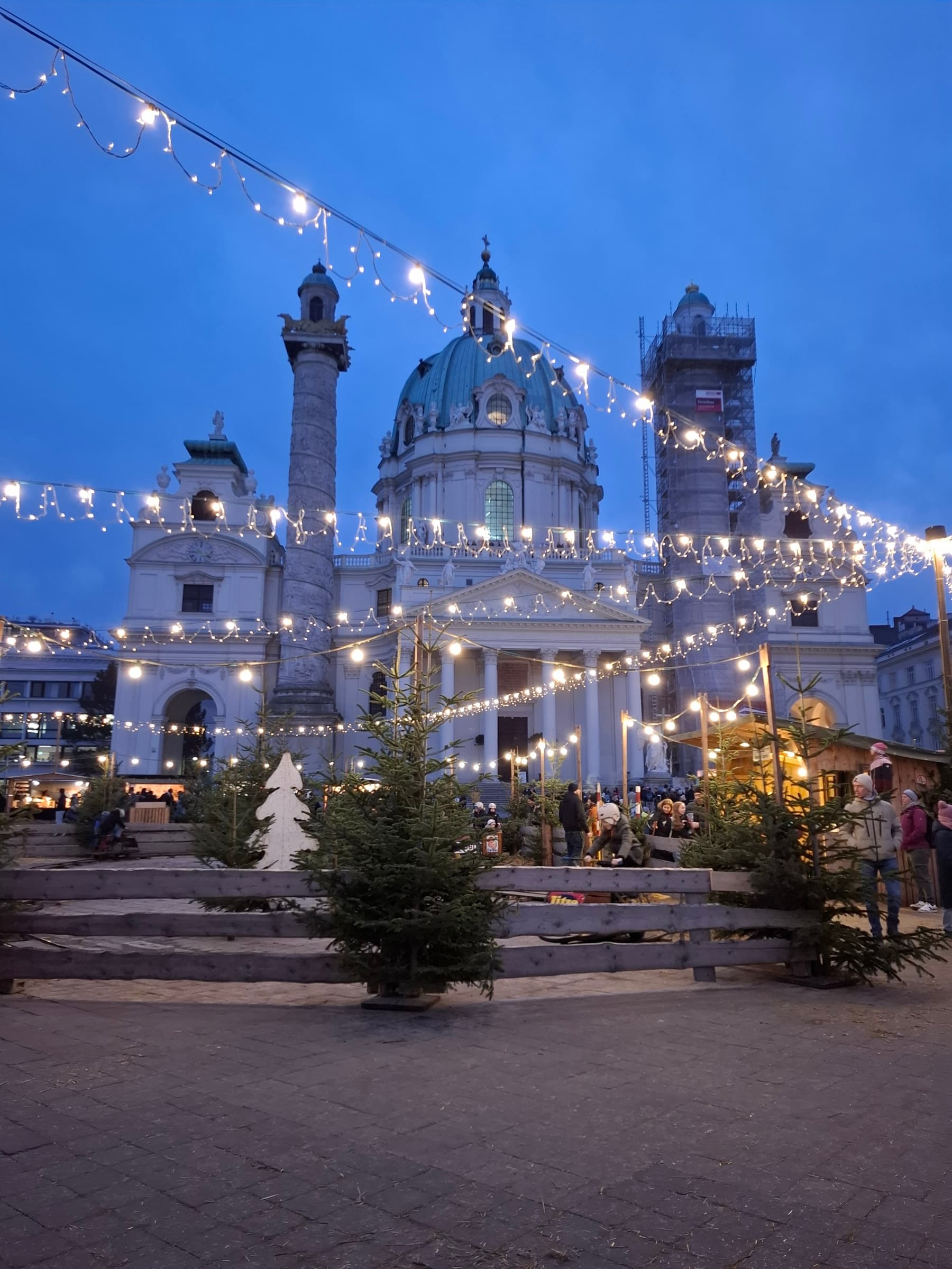 Karlskirche in Vienna lit up at dusk above the Christmas market